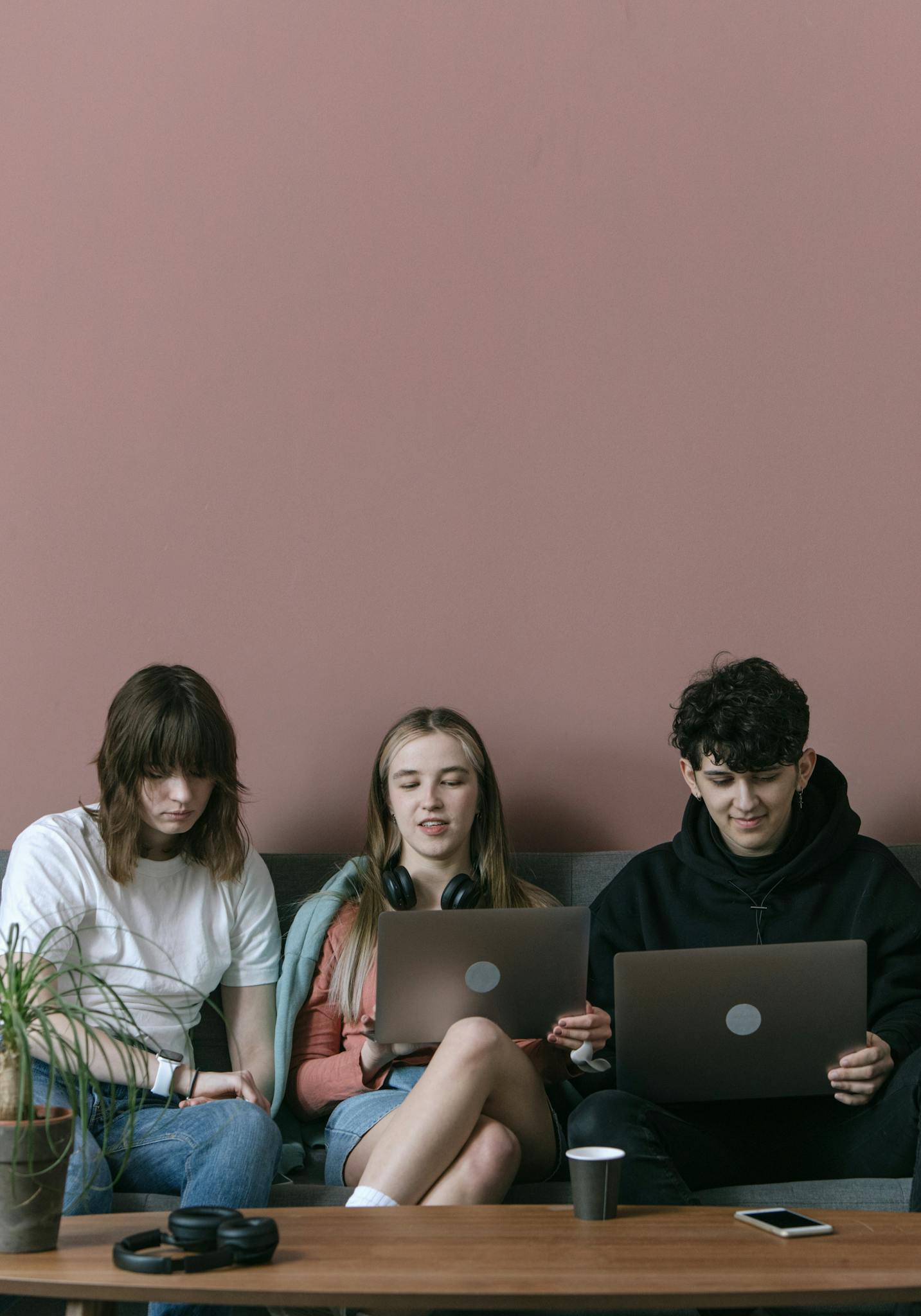 Three young adults sitting indoors working on laptops, casual setup.