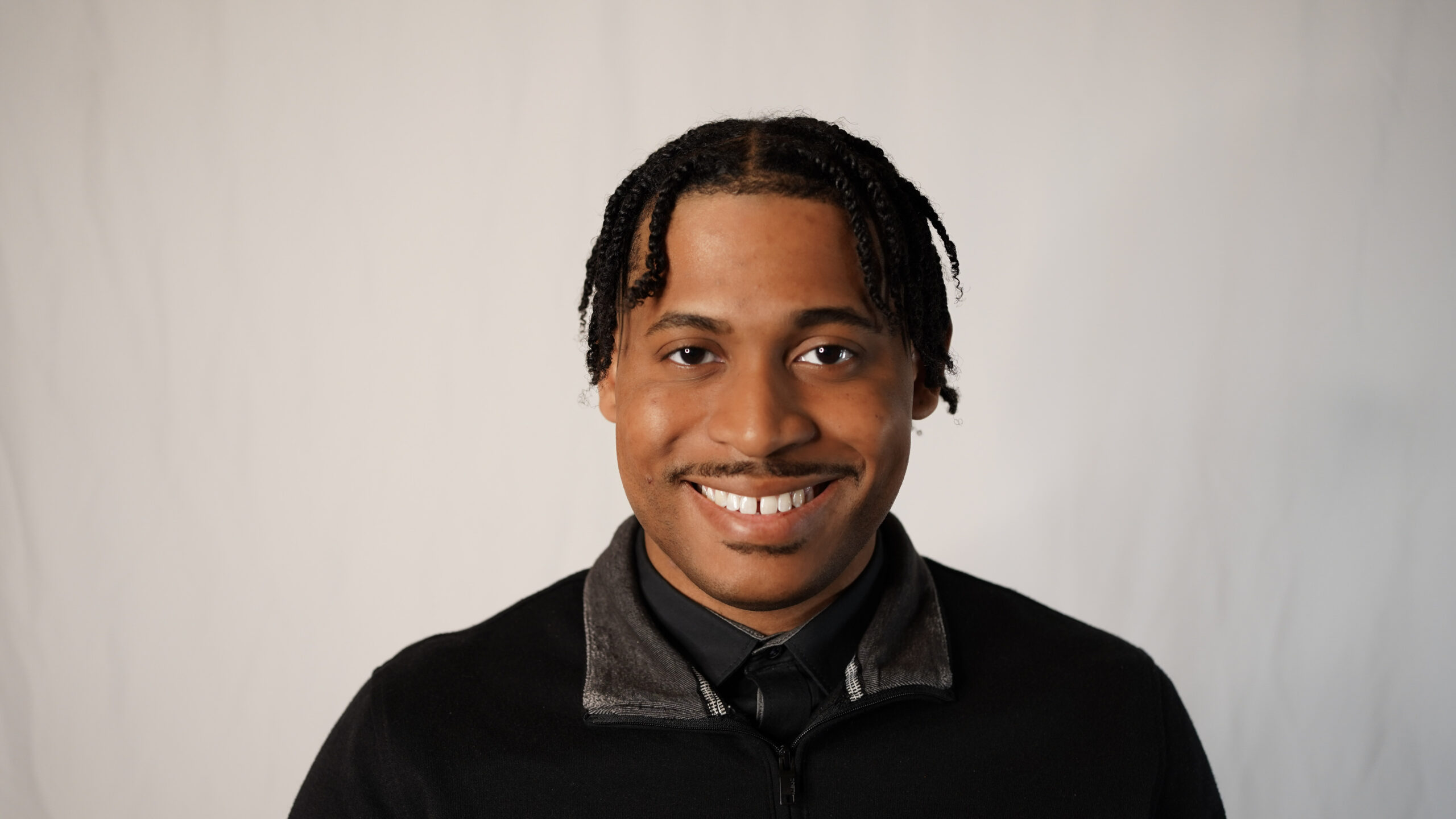 Tyler Jurelle smiling in a black quarter-zip sweater against a light gray backdrop.